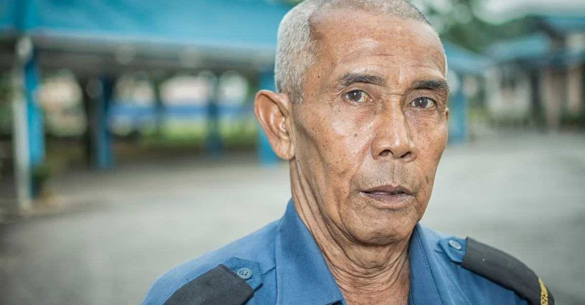 Portrait d'un agent de sécurité âgé portant un uniforme bleu à l'extérieur, montrant vigilance et dévouement.