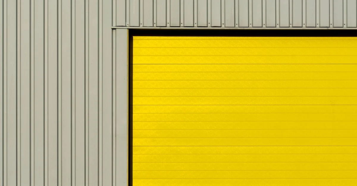 Gros plan d'une porte de garage moderne avec revêtement jaune et murs en métal gris ondulé.