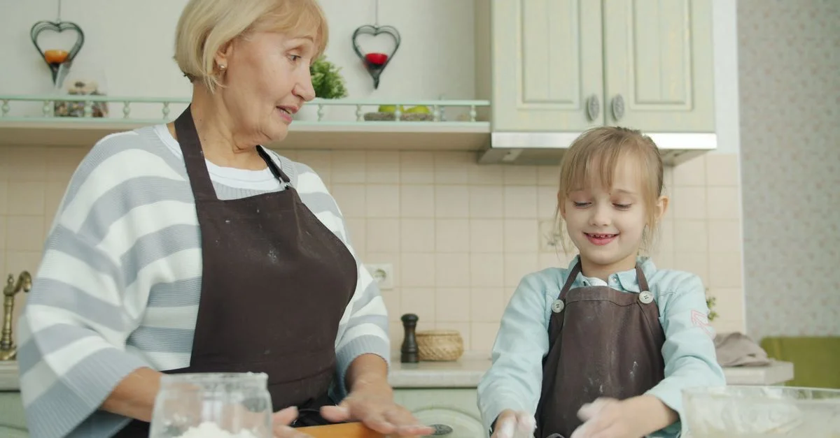 Une femme âgée et une jeune fille font de la pâtisserie dans la cuisine, portant des tabliers.