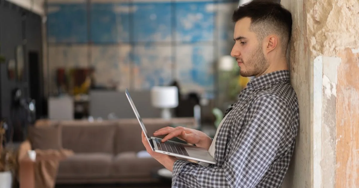 Homme travaillant sur un ordinateur portable debout à l'intérieur avec un arrière-plan de bureau moderne. Idéal pour des thèmes d'affaires et de technologie.