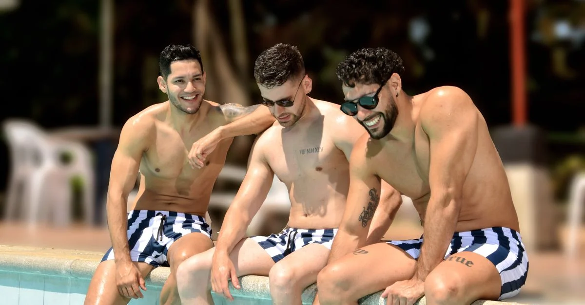 Trois jeunes hommes en maillots de bain rayés profitant d'une journée ensoleillée au bord de la piscine, souriants et détendus.