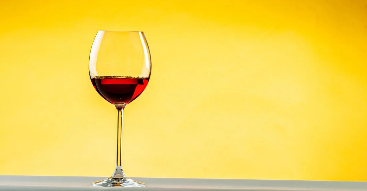 Image minimaliste d'un gobelet de vin avec du vin rouge sur un fond jaune vif.