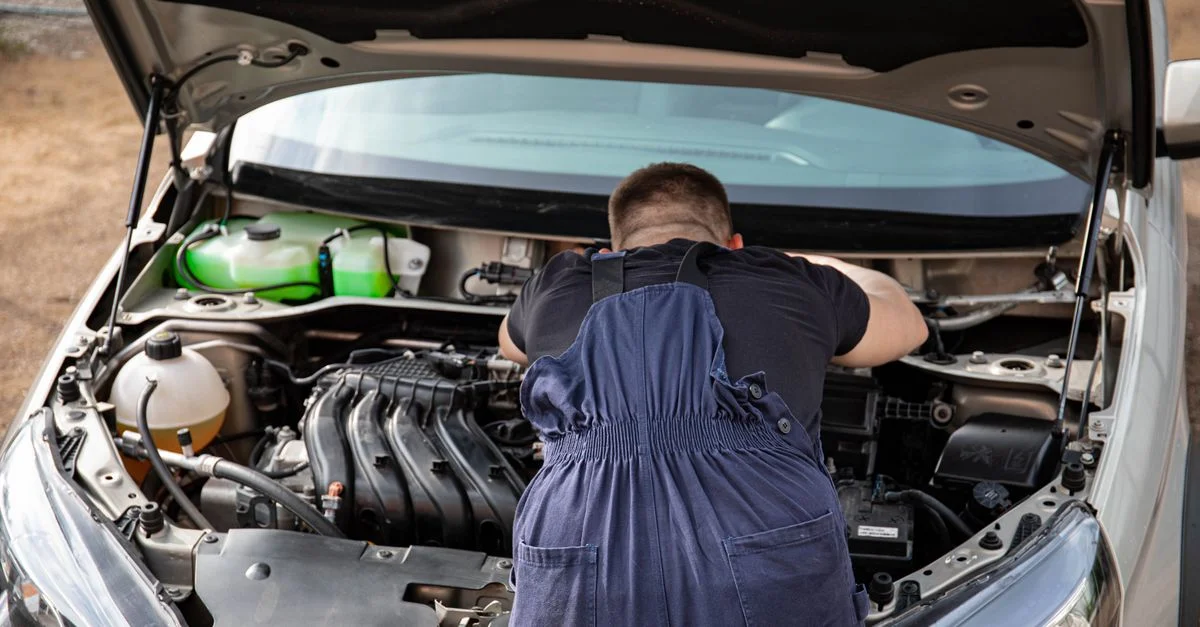 Mécanicien en bleu de travail travaillant sur un moteur de voiture à l'extérieur, vue de dos.