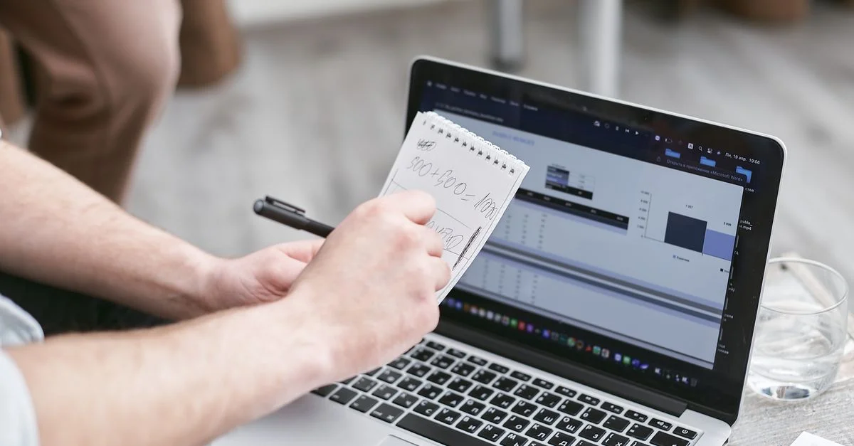 Personne analysant des données sur un ordinateur portable tout en prenant des notes, se concentrant sur les tendances du marché.