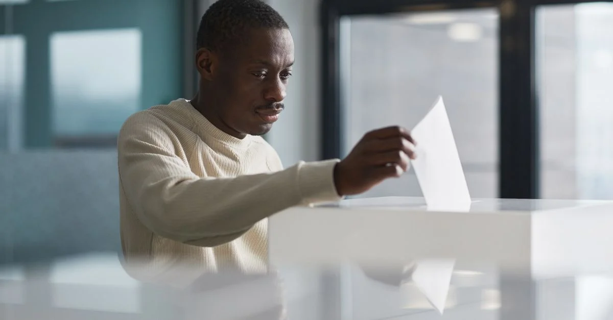 Un jeune homme déposant son vote dans un bureau de vote intérieur, concentré sur le processus démocratique.