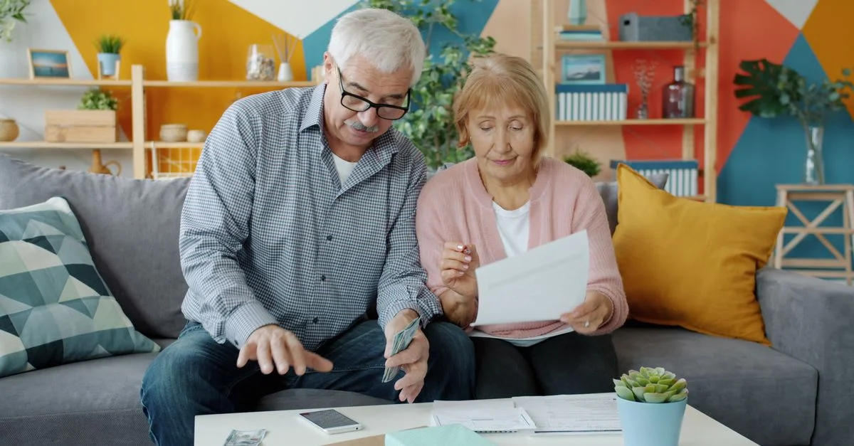 Un couple de personnes âgées établit son budget, en consultant des documents dans un salon confortable.