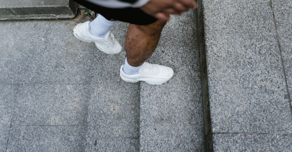 Personne portant des baskets blanches montant des escaliers en pierre grise en extérieur.
