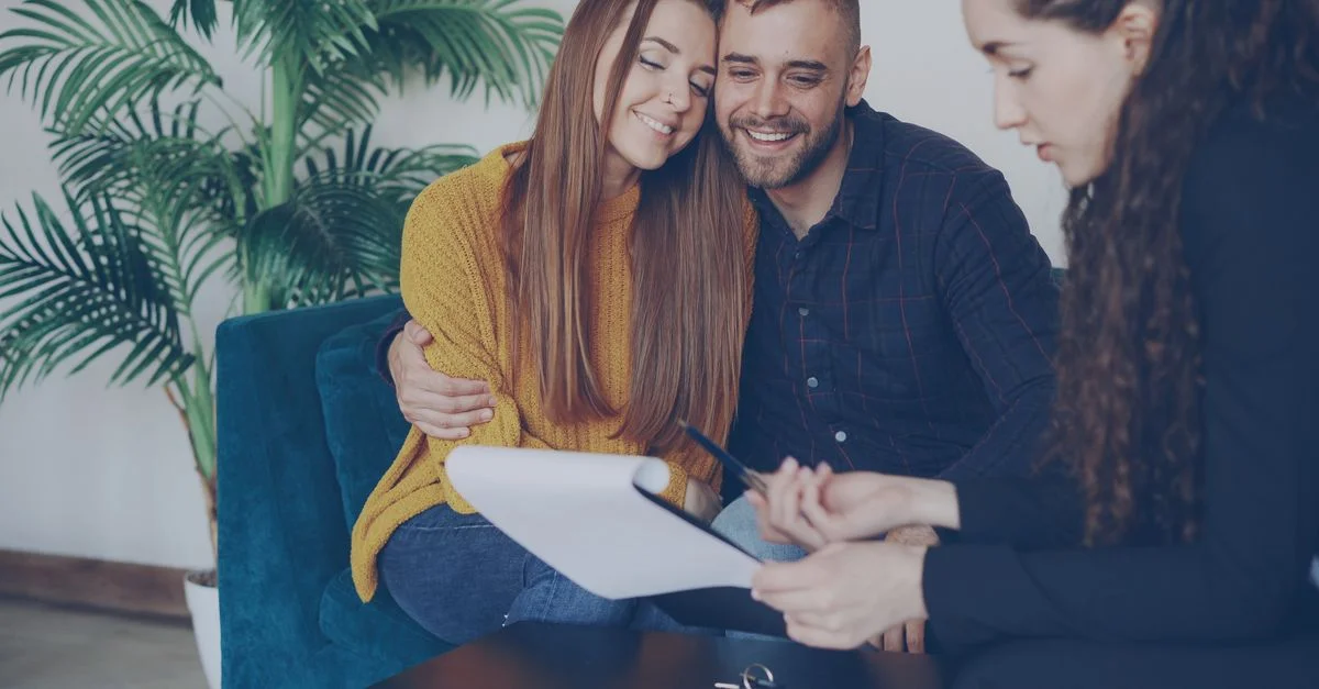 Un couple souriant consulte un conseiller dans un bureau à l'ambiance chaleureuse.