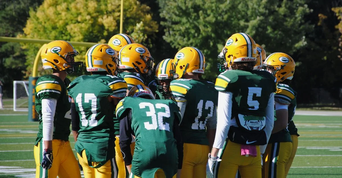 Équipe de football américain au lycée en uniformes verts se regroupant par une journée ensoleillée.