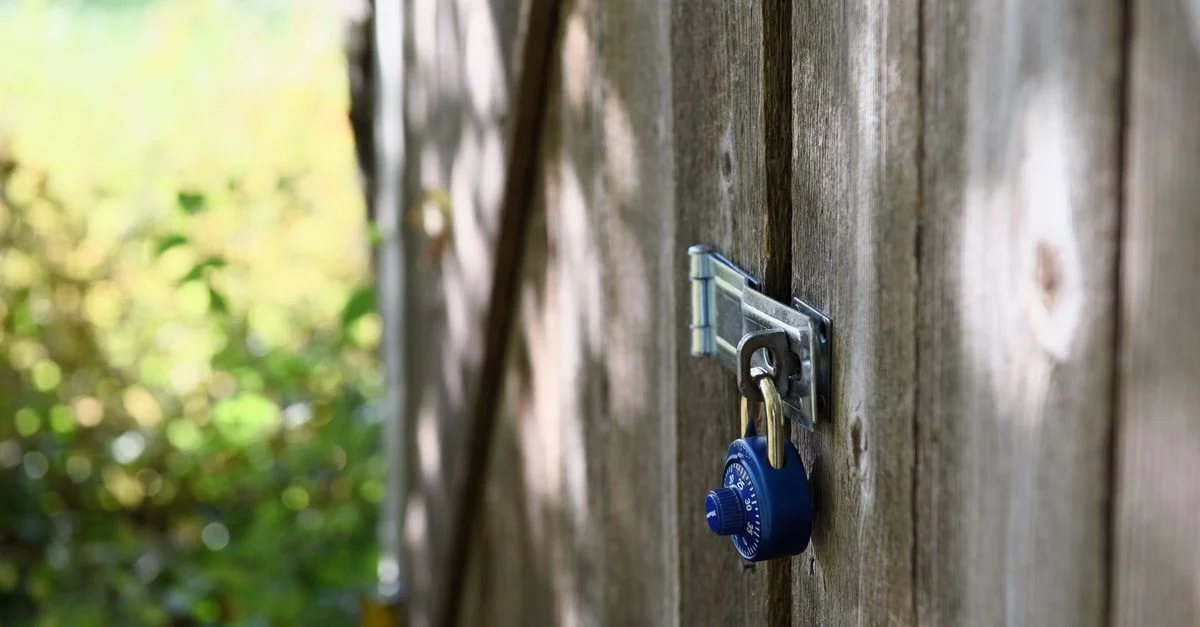 Un cadenas bleu sécurise une porte en bois à l'extérieur, avec la lumière du soleil qui filtre à travers.